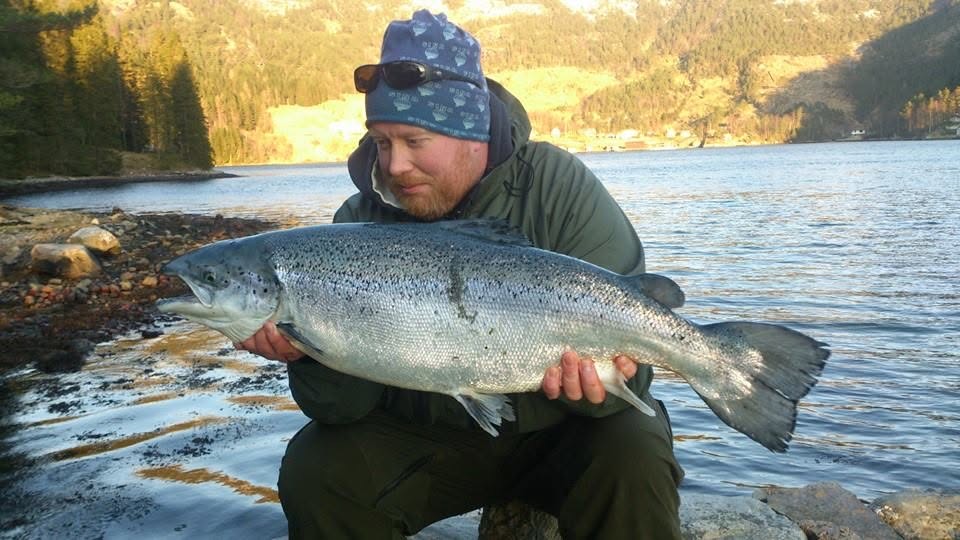 Fisker sitter i fjæra med en stor laks i hendene